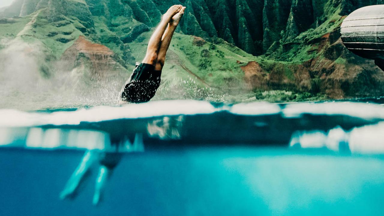 Man jumping in ocean from boat in Kauai