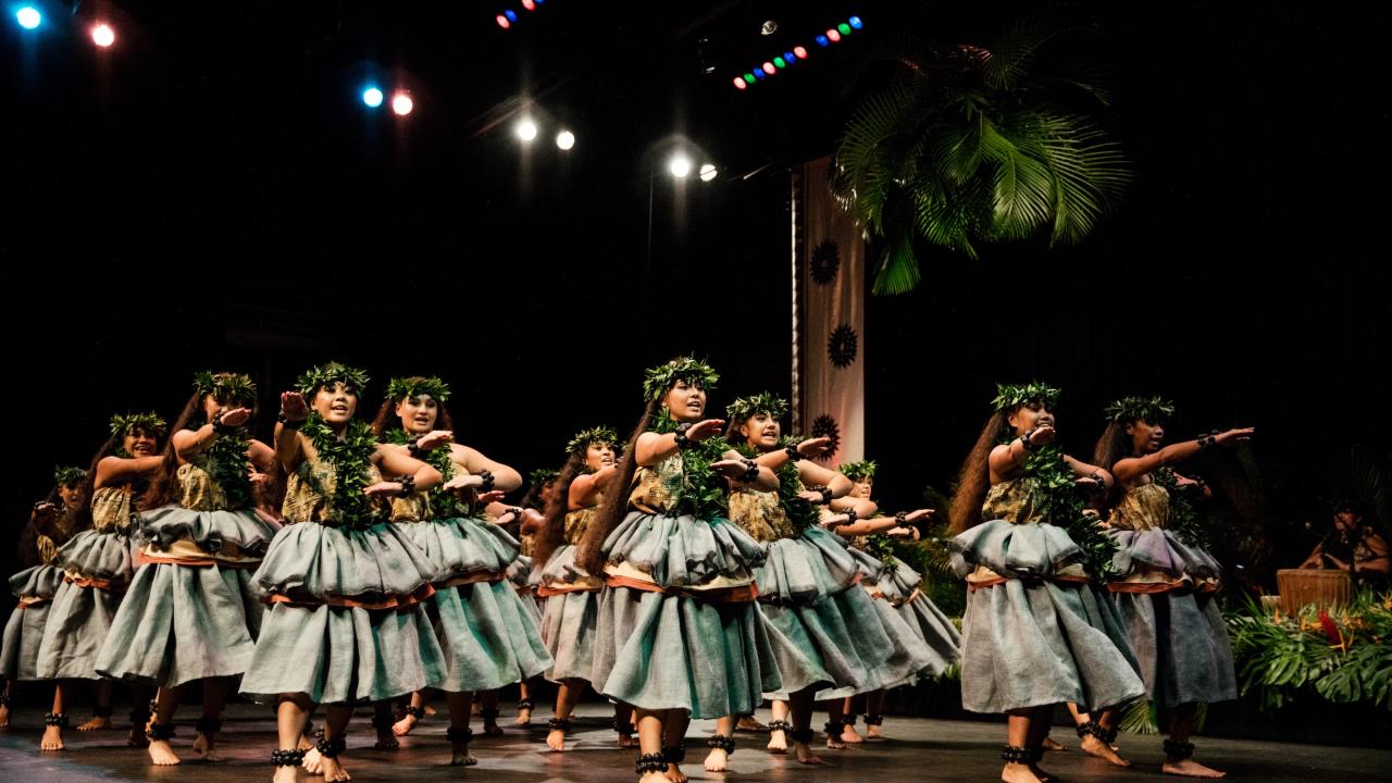 Group of women in traditional Hawaiian dress on stage dancing