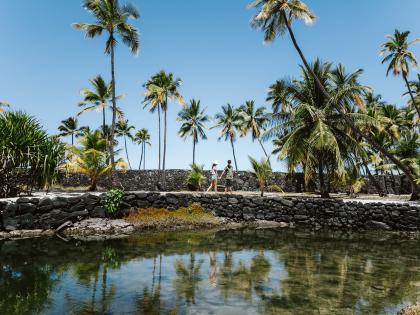 Couple walk along path near a Puuhonua o Honaunau fishpond