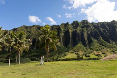 Bride and groom walk in a valley with views of the Koolau mountains