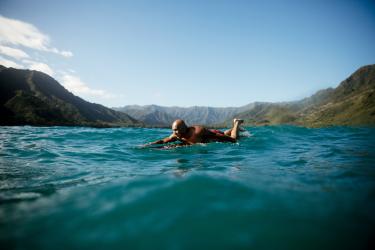 Tom Pohaku Stone paddling out on a surfboard