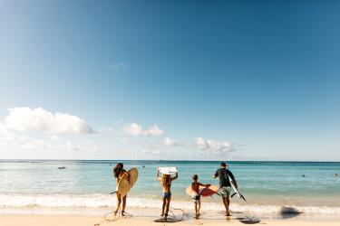 four people carrying surfboards into the ocean