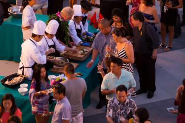 chefs at a table serving food to many surrounding guests